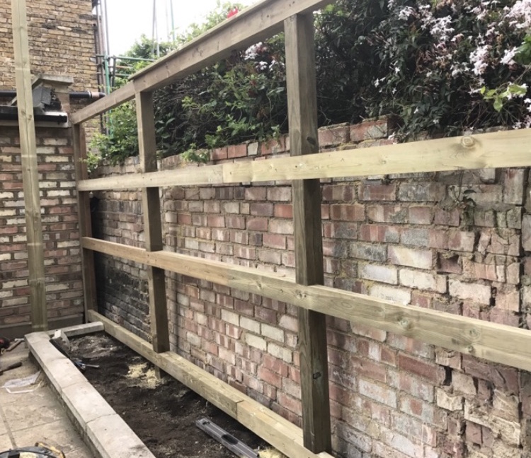 Timber posts and horizontal rails being installed alongside a brick wall.