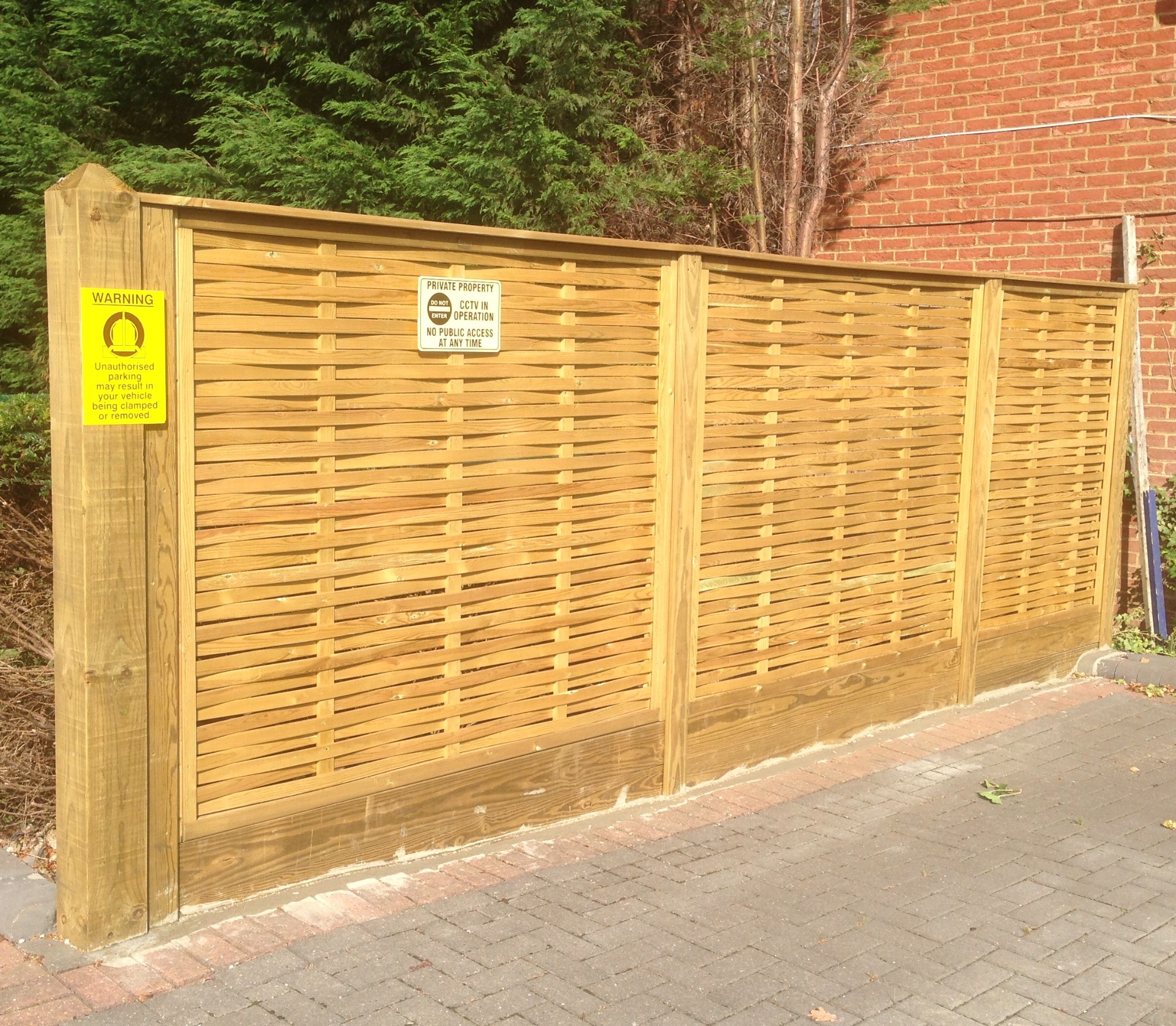 Woven timber panels beside a paved area and brick wall.